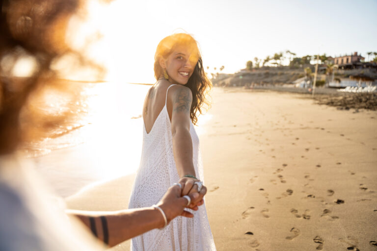 couple-walk-along-beach-woman-looks-back.jpg